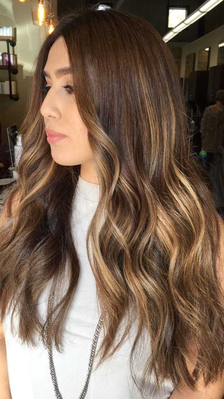 Woman with long, wavy, brown hair with highlights in a salon.