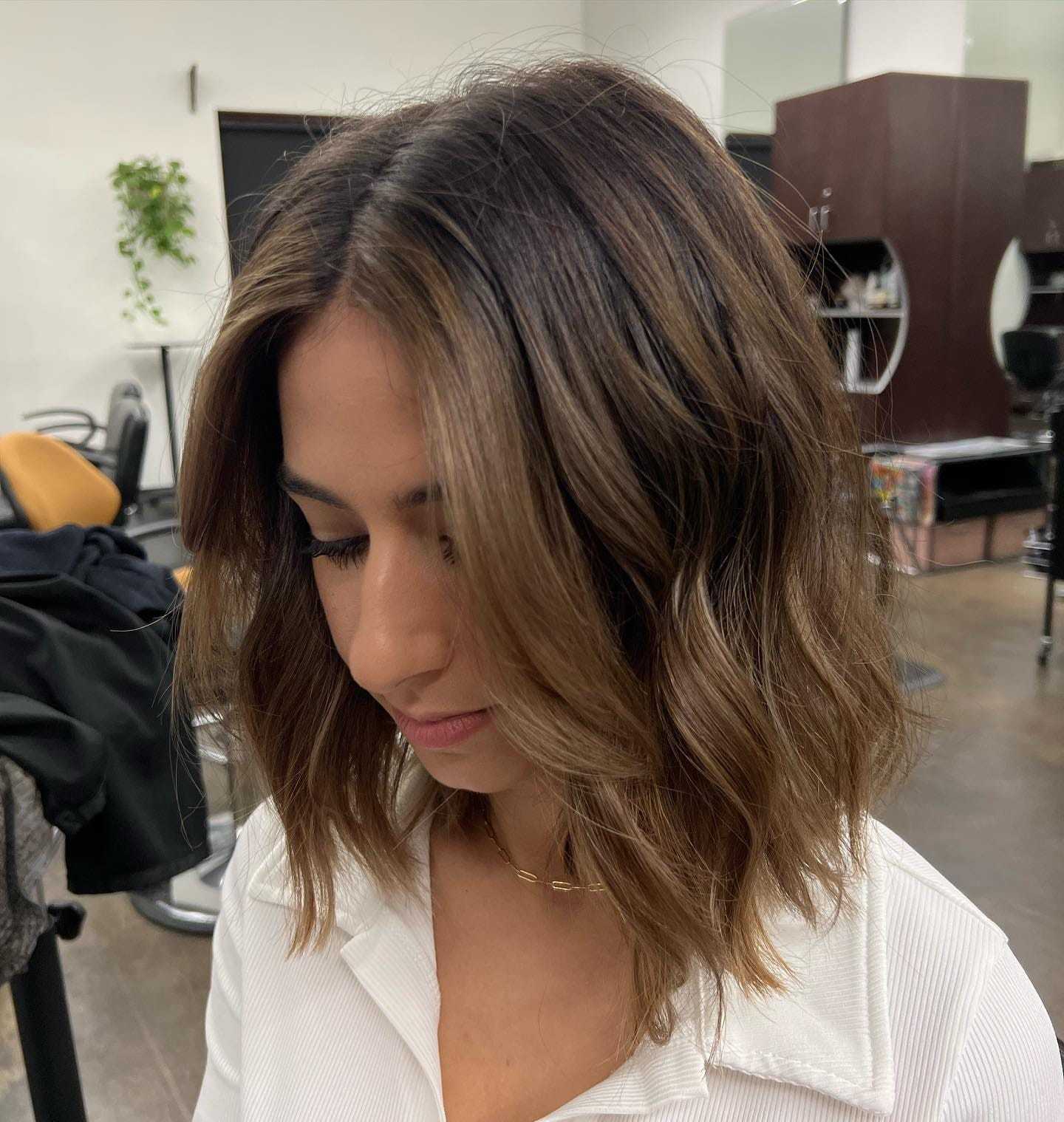 Woman with shoulder-length wavy hair and face-framing highlights in a modern salon.